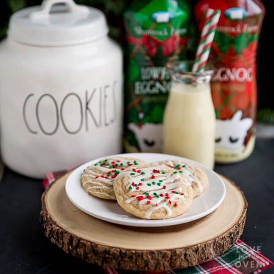 A plate of cookies styled on a wooden round with a cookies jar in the background alongside bottles of eggnog.