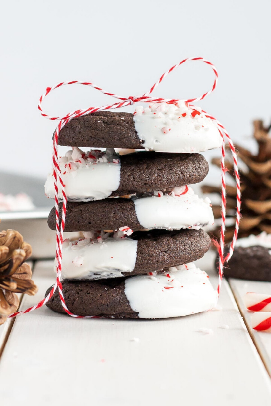 Stack of five dark chocolate cookies half-dipped in white chocolate with crushed peppermint on top and tied up with candy cane string.