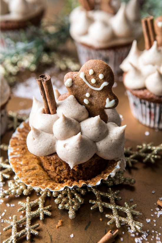 A cupcake with the wrapper pulled back and topped with dollops of frosting, a cinnamon stick and a fresh-baked gingerbread man.