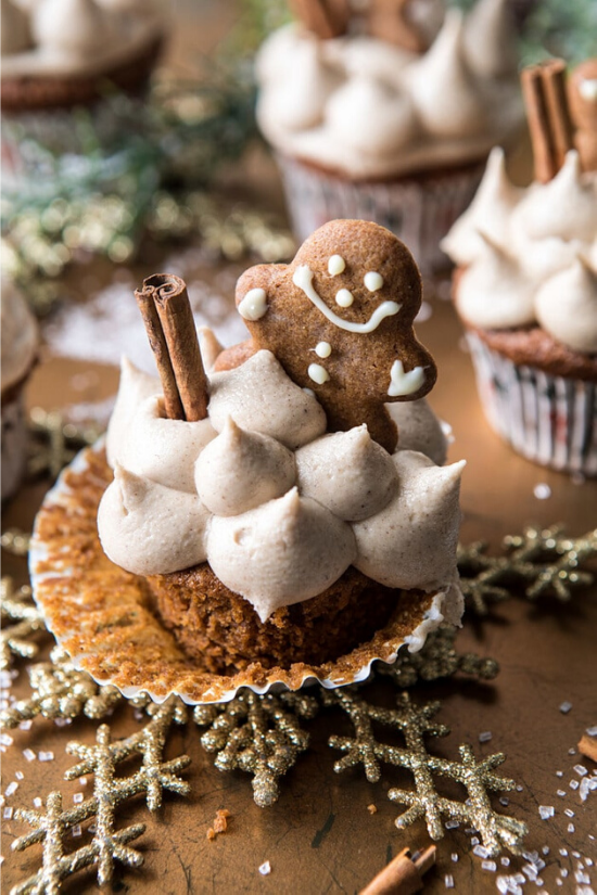 A cupcake with the wrapper pulled back and topped with dollops of frosting, a cinnamon stick and a fresh-baked gingerbread man. 