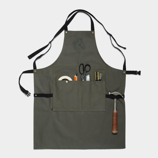 Slate gray utility apron with metal accents and black ribbon ties, pockets filled with scissors, hammer tape and other odds and ends, the perfect guy gift.