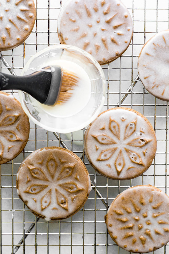 Pastry brush glossing over cookie stamped snowflake gingerbread cookies with white glaze.