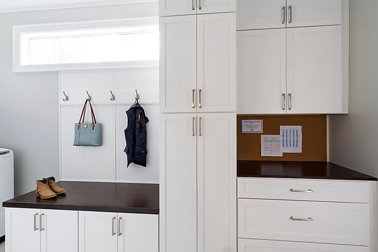 White cabinetry in a customized mudroom with long rectangular window, hanging hooks and cork board. 