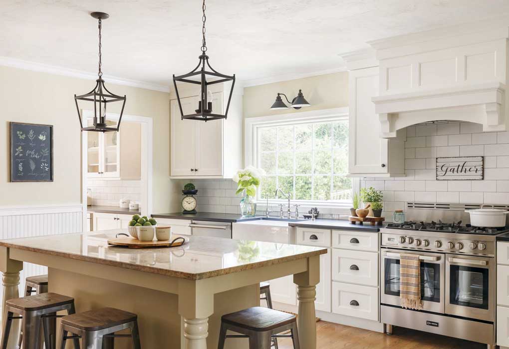 Large custom kitchen island with dark pendants hanging above and rustic farmhouse accents throughout the kitchen. 