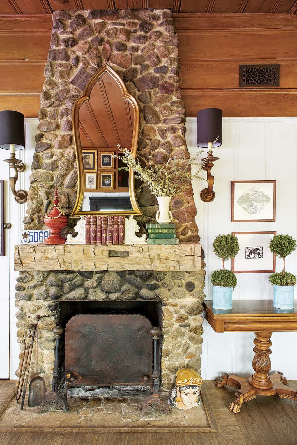 Floor to ceiling stone fireplace with a distressed wooden mantle and a gold-trimmed mirror above it. 