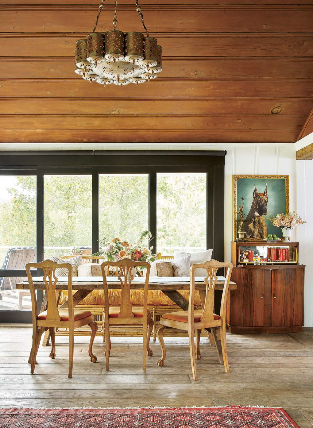 Handmade wooden dining table surrounded by intricate dining chairs, looking out a large wall of windows next to a fold down bar. 