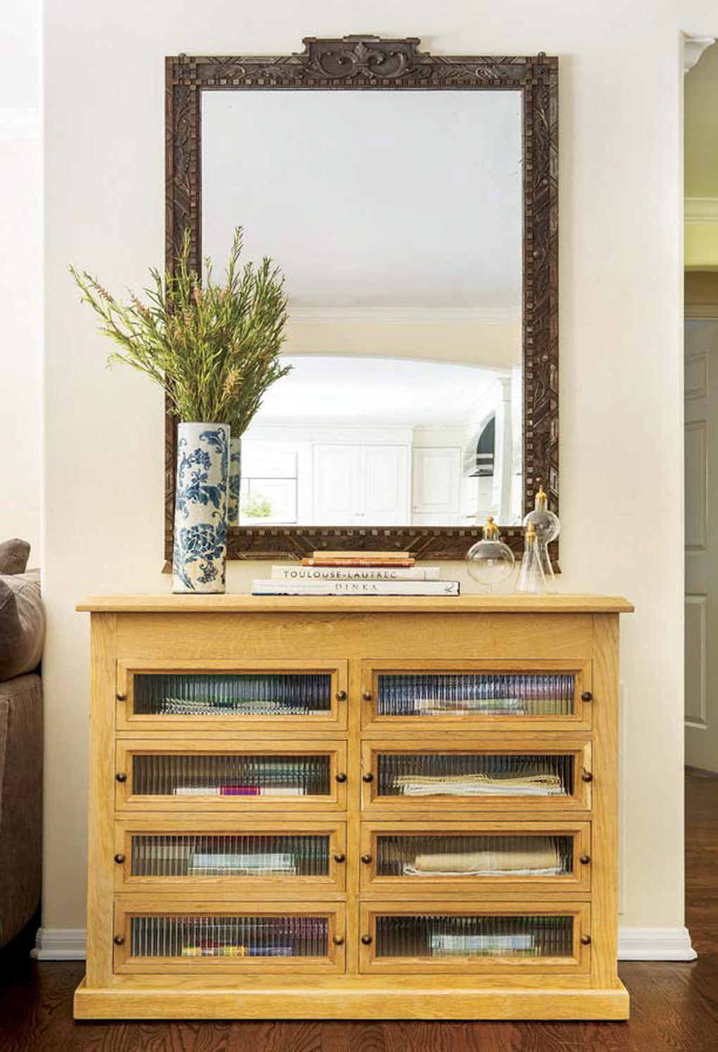 Custom made cabinet with muted glass panels topped with an ornate mirror mounted to the wall. 