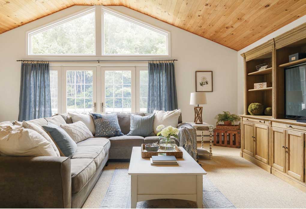 A family room, with a vaulted, wood-paneled ceiling and a large sectional facing a full wall media setup. 