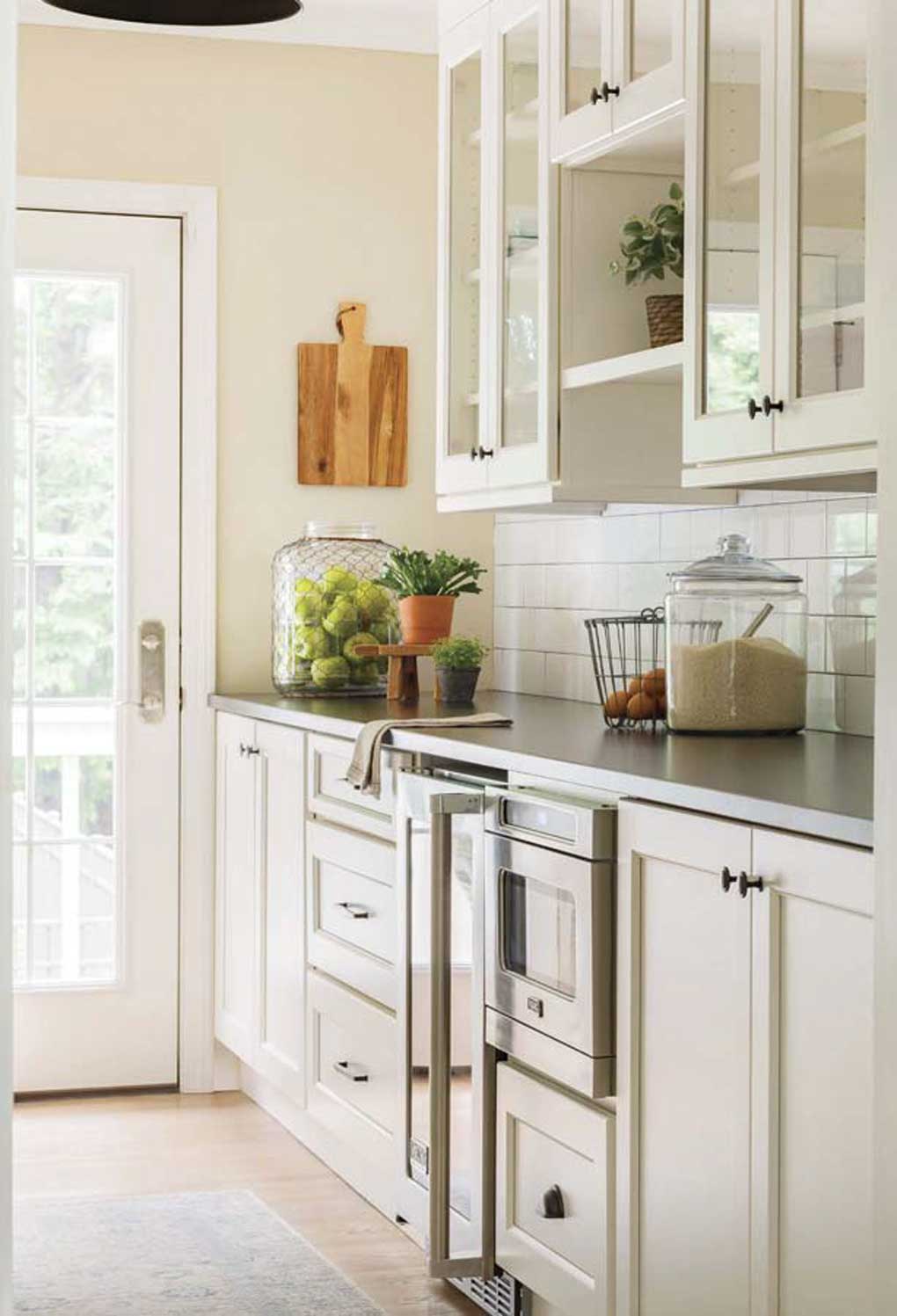 Creamy white kitchen, near a glass paneled back door letting in tons of light and small plants giving texture to the countertops. 