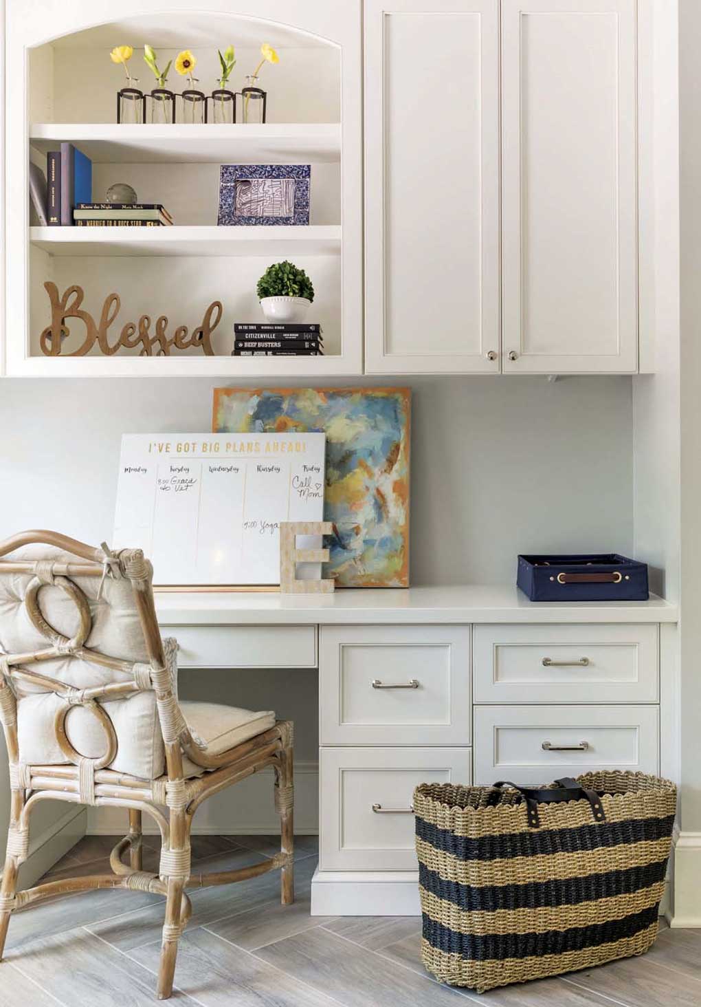 White cabinetry in a home office with a rattan styled chair next to a woven shoulder bag. 