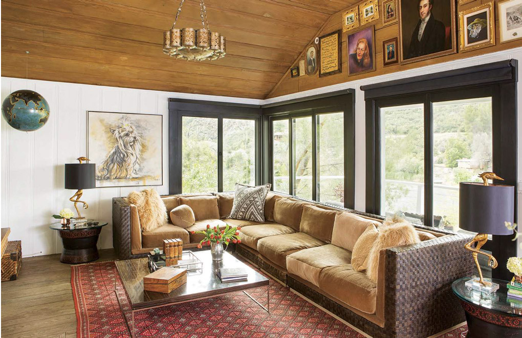 Living space with a wall of windows behind the sectional with a unique chandelier, lake house decor and a collection of portraits above the windows. 