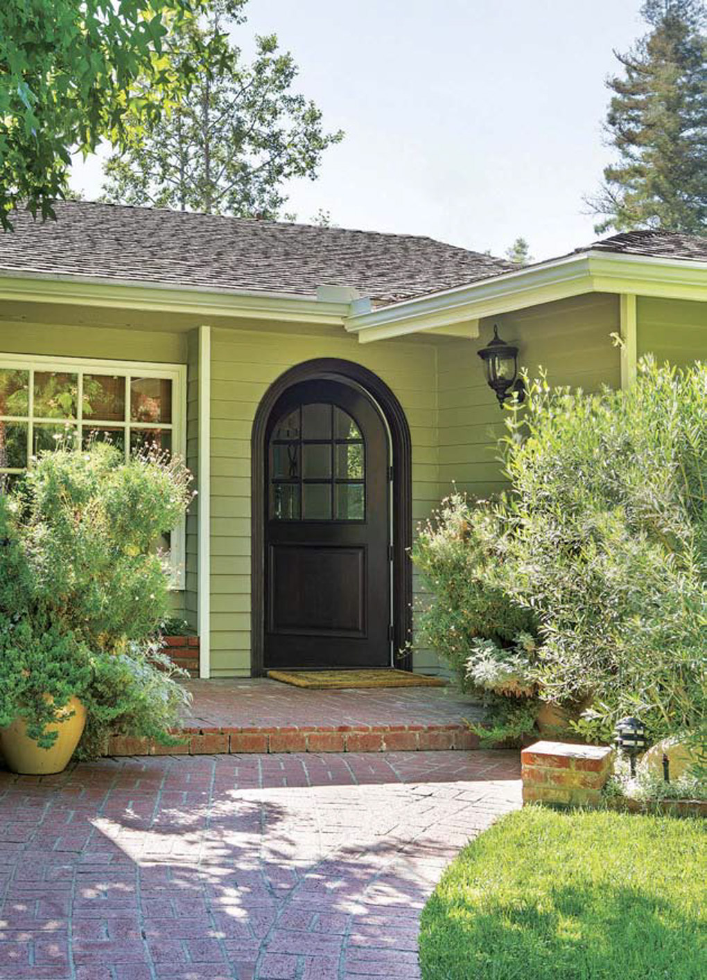 Brick paved front walkway up to a green home with an open rounded black front door. 