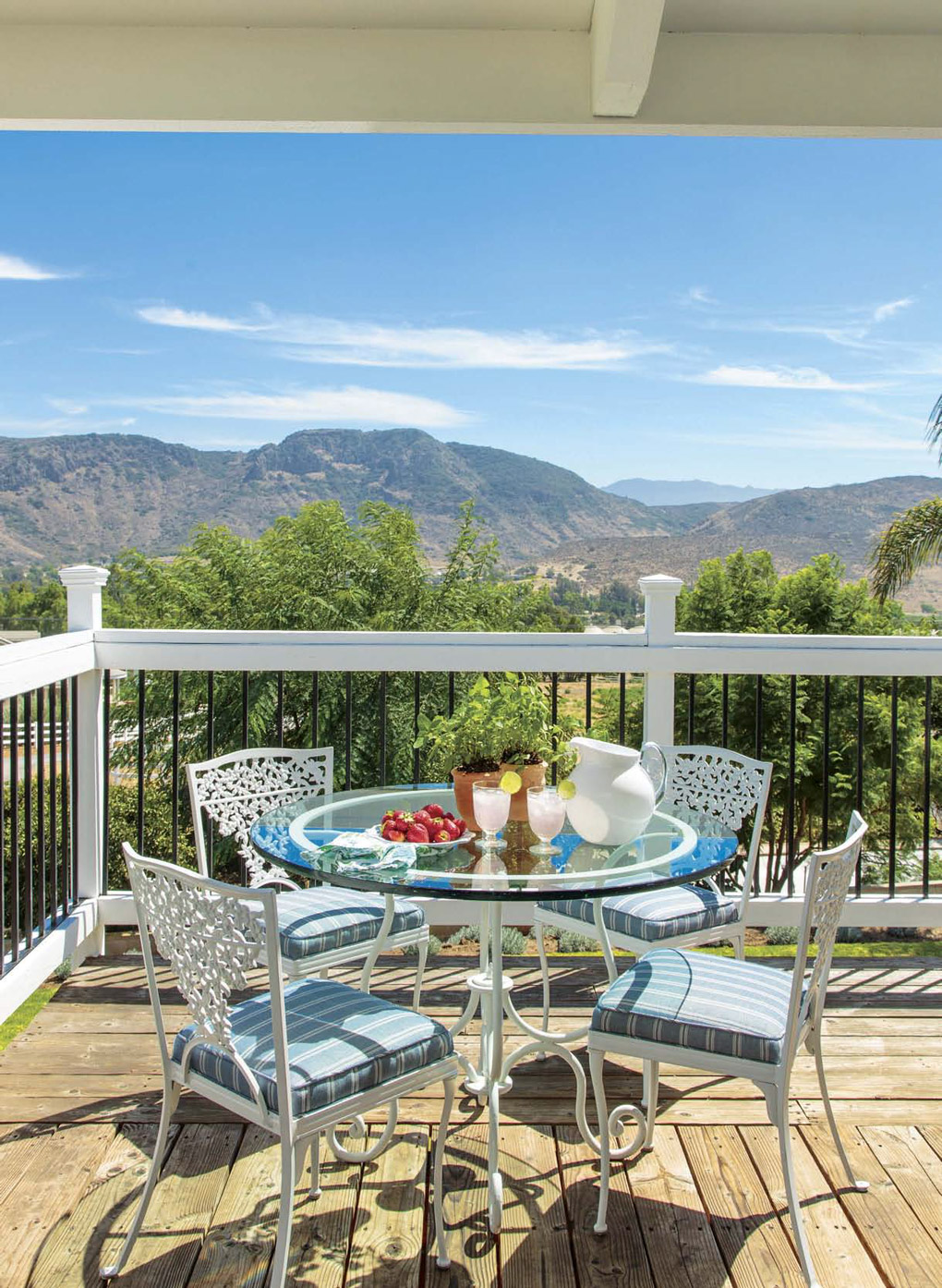 Wrap around deck with white metal dining bistro set arranged for a fresh breakfast with a view of expansive mountains. 