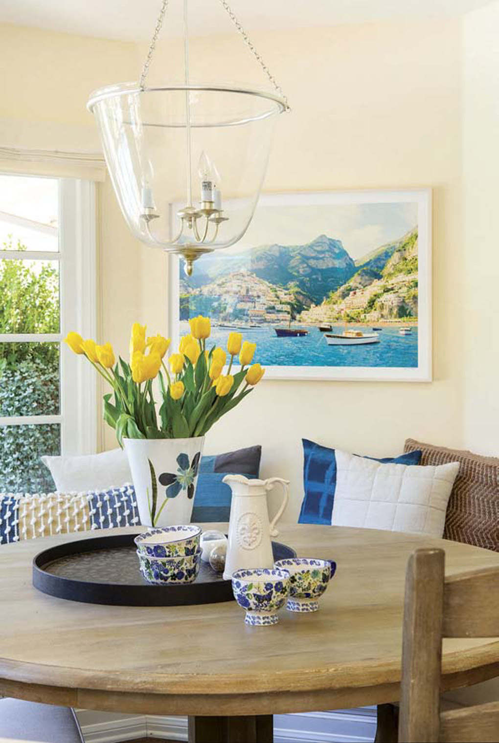 Round, pedestal kitchen table topped with yellow tulips in a vase with banquette seating. 