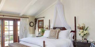 Master bedroom with a wooden carved four-poster bed topped with white linens and hanging mosquito netting as decoration.