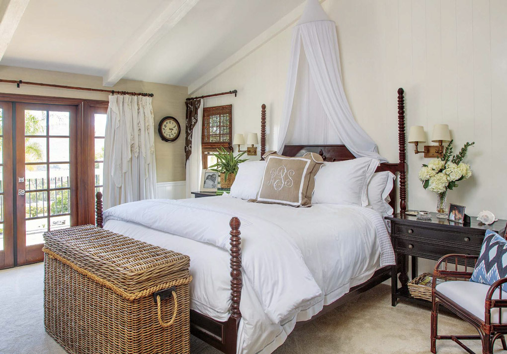 Master bedroom with a wooden carved four-poster bed topped with white linens and hanging mosquito netting as decoration. 