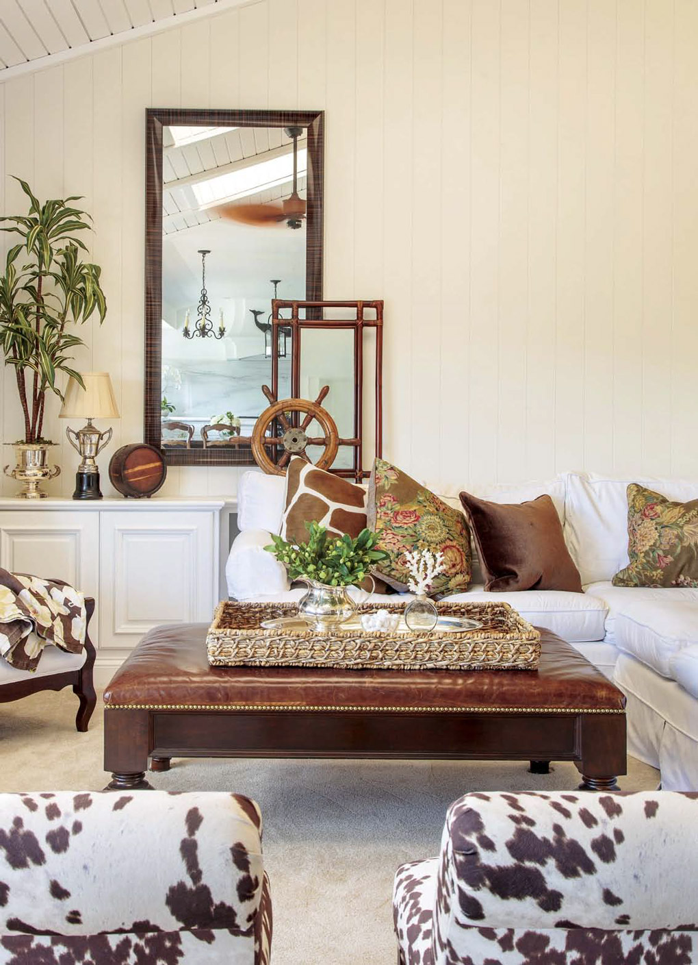 Light and bright family room with large leather topped ottoman, light colored couches and touches of warn brown tones and faux animal-hide textures. 