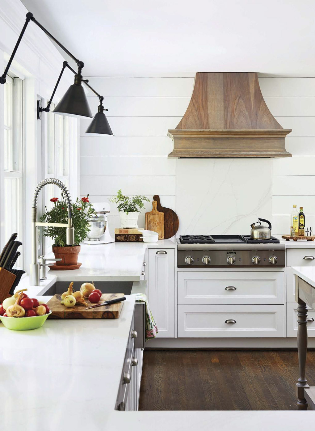 White kitchen with modern farmhouse lights above the sink and a custom wooden range hood. 