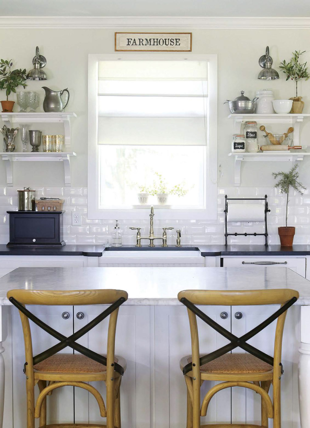 White kitchen renovation looking over two wooden barstools at the brightly lit center window flanked by white floating shelves. 