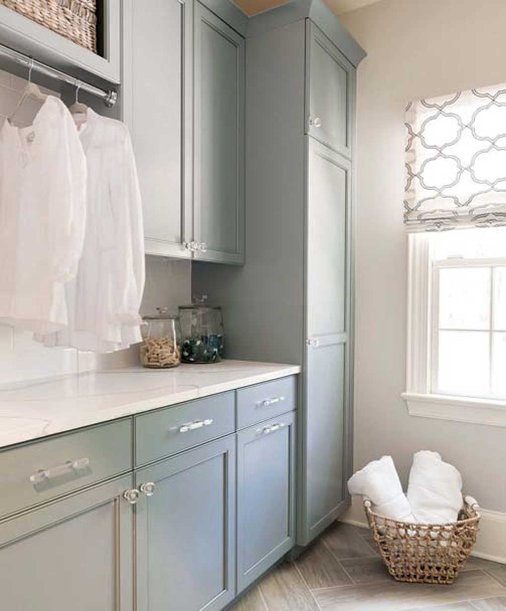 Clean and crisp laundry room with tile floor, blue cabinets and a wicker basket filled with white towels. 