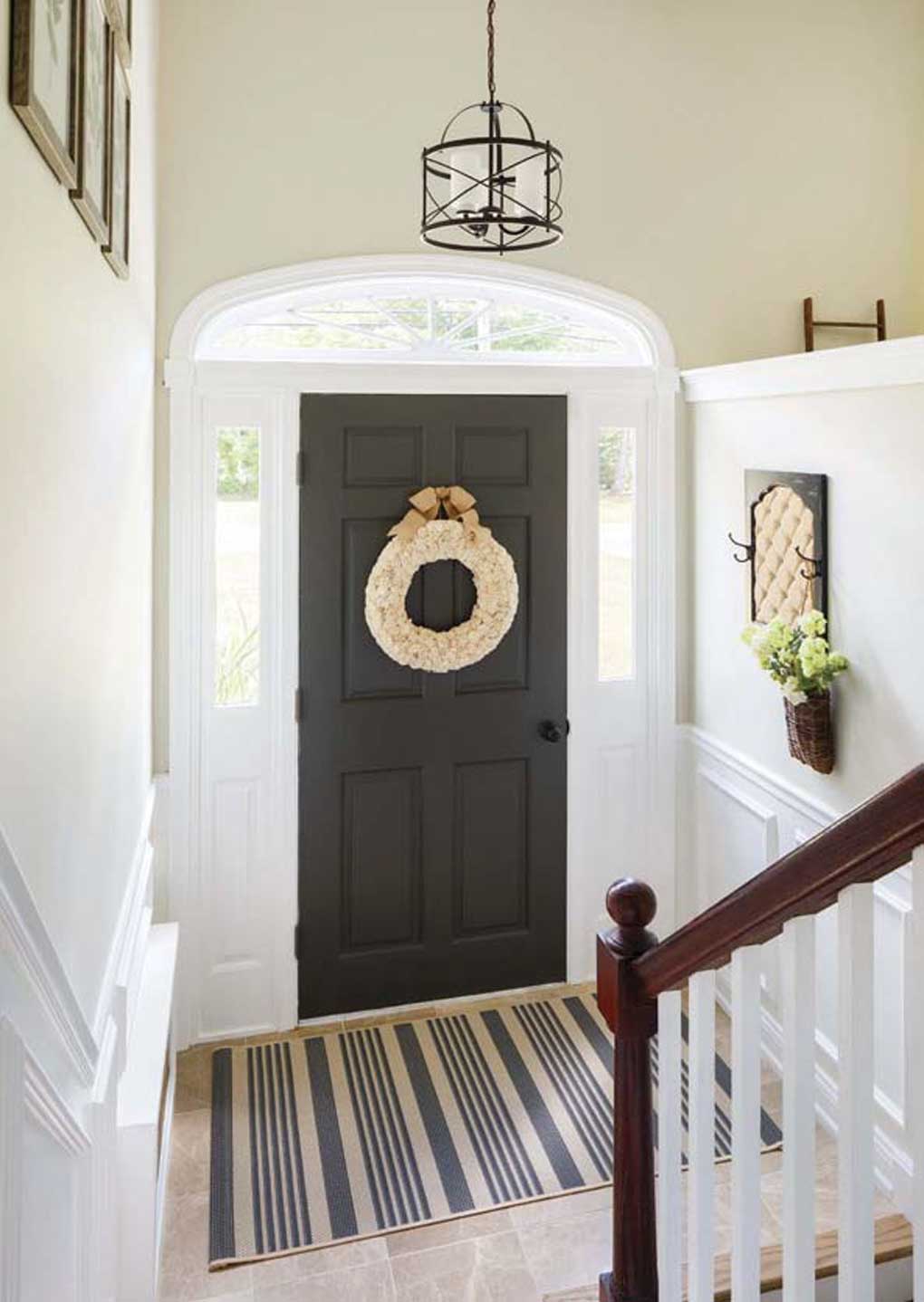 Large foyer with a hanging pendant lamp, beige floor tile and a black front door with a wreath. 