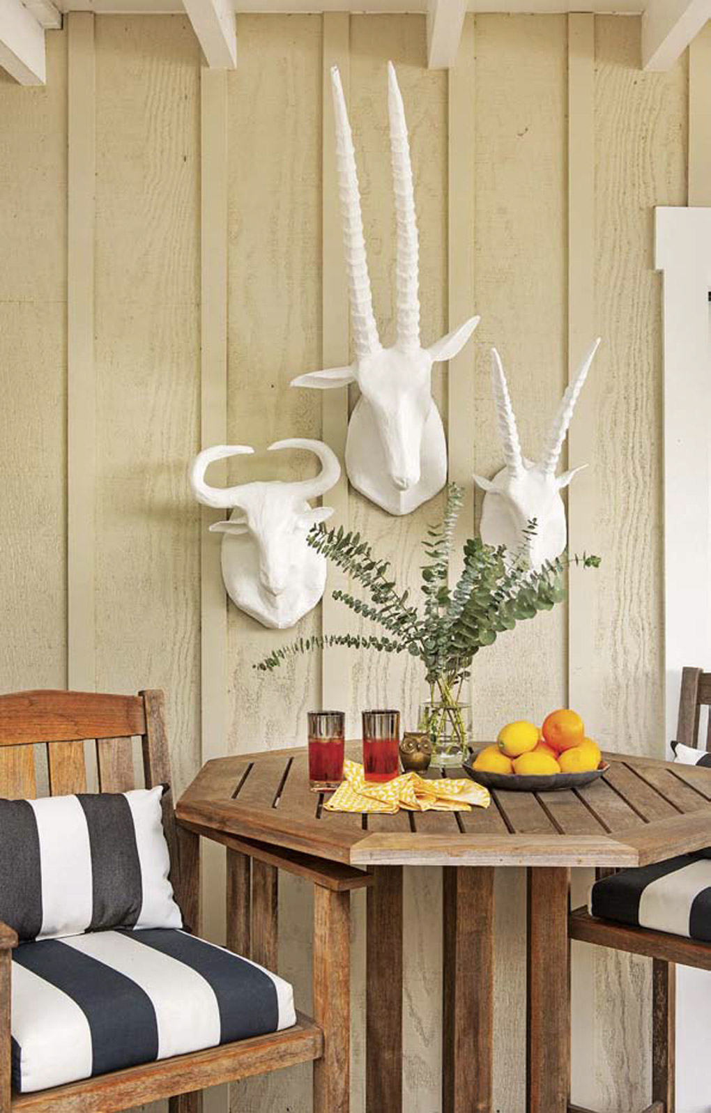 Outdoor teak bistro set with black and white striped cushions and set with a snack prepared in the table with white faux animal wall mounts on the wall. 