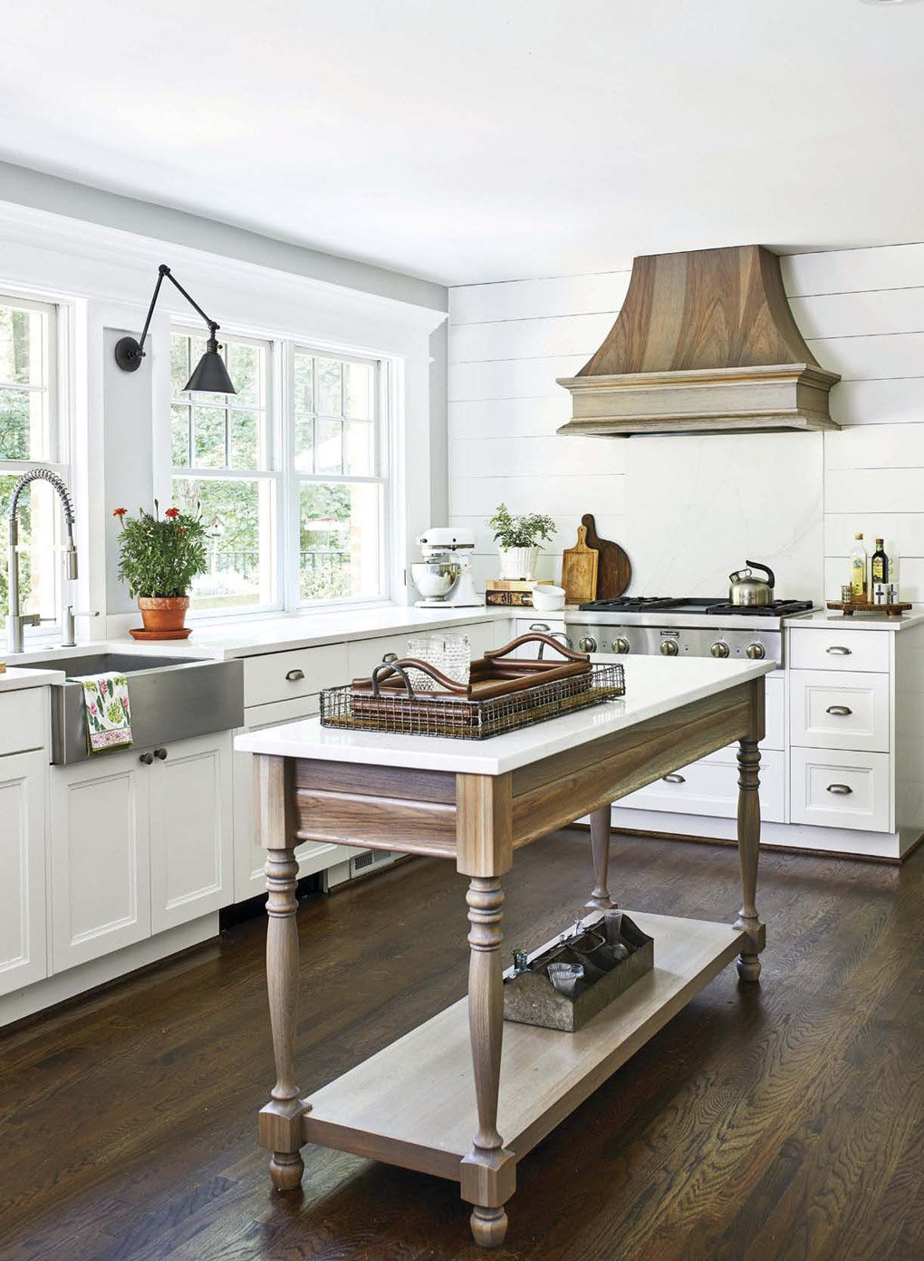 Custom designed island with turned wooden legs and all white kitchen counter and cabinetry in the background.