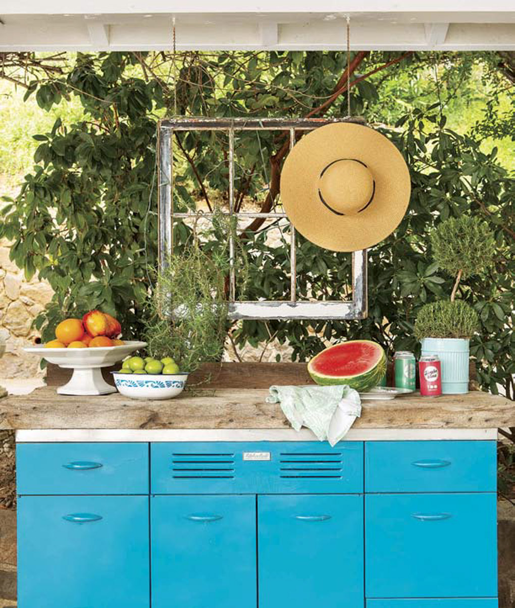 Bright blue vintage metal cabinets made by Kraft Maid placed on the lake house deck with a wooden top and a hanging vintage window above it. 