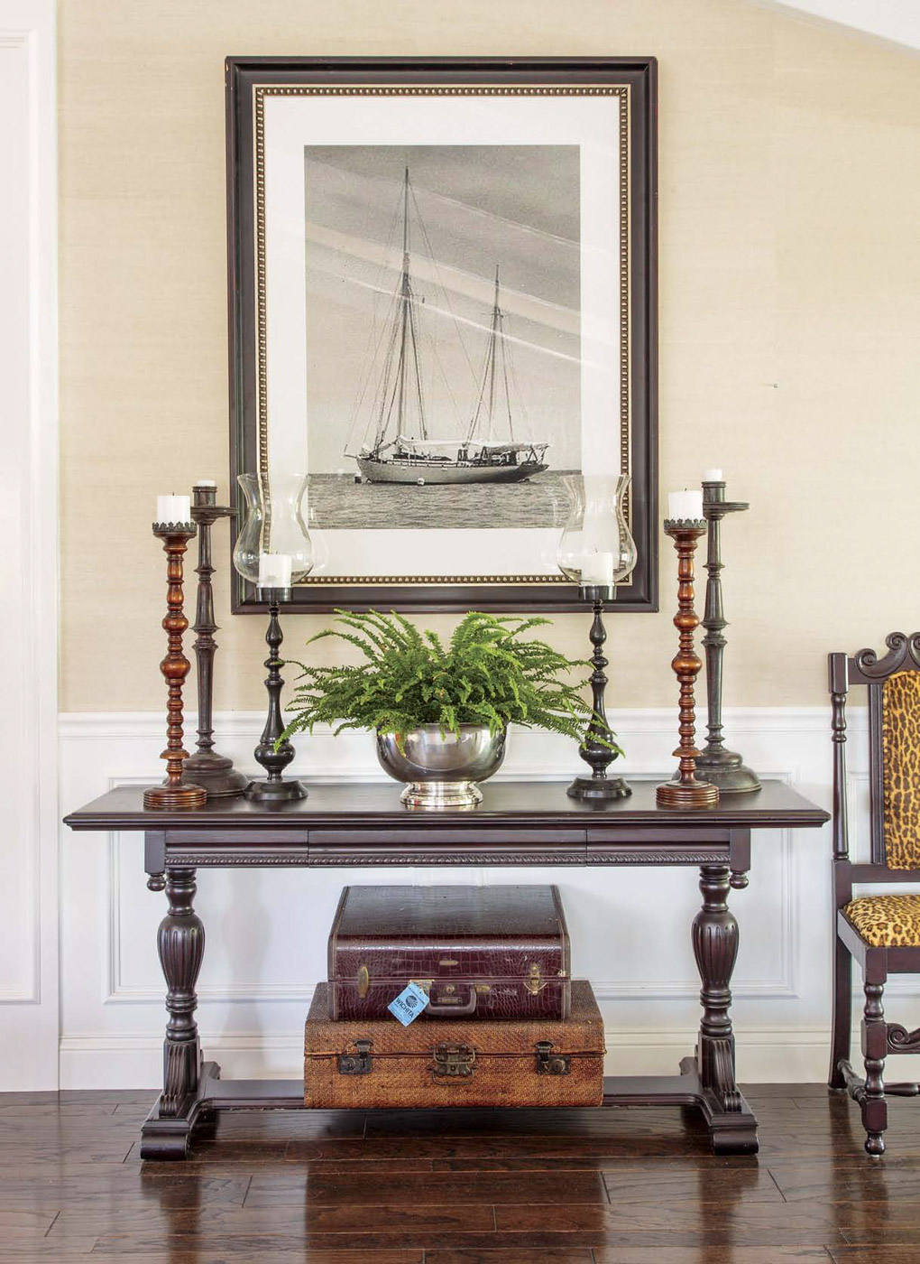 Antique wooden console in the entryway topped with tall candlesticks and a fern, also displaying vintage suitcases underneath. 