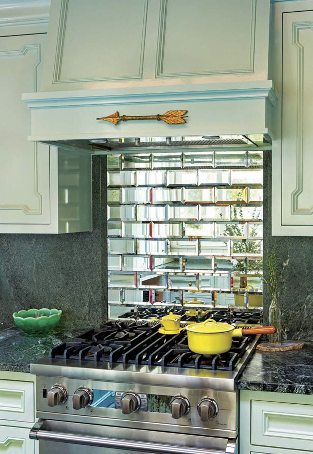 Small stainless steel range with a mirrored subway tile backsplash surrounded by light aqua colored cabinets. 