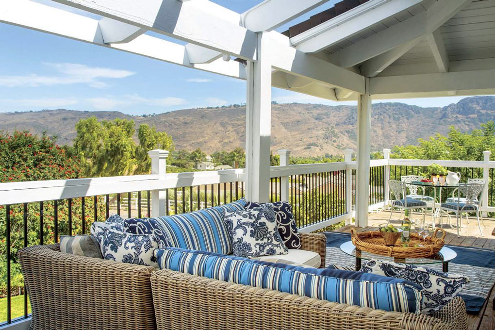 Outdoor deck seating area with open pergola and rattan style sectional with blue accent cushions. 