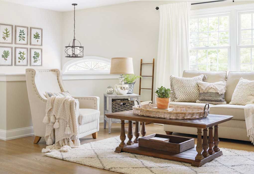 Bright and light neutral living room with oatmeal colored couch and armchair, wooden accent furniture and mercury glass lamp all on a light colored shag rug.