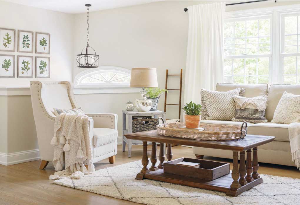 Bright and light neutral living room with oatmeal colored couch and armchair, wooden accent furniture and mercury glass lamp all on a light colored shag rug. 