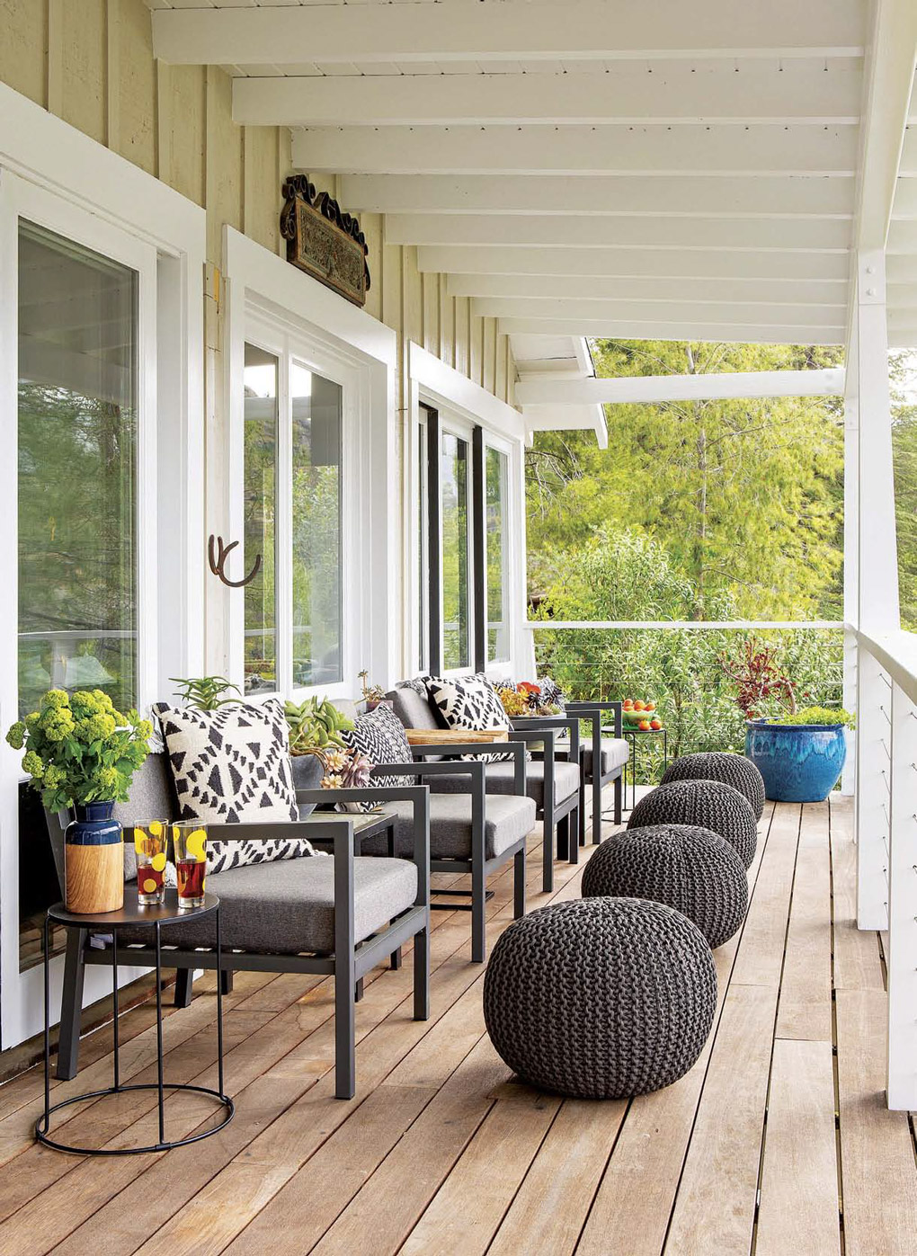 Lake house deck with wire railings in white and decorated with gray outdoor chairs and matching poufs as foot rests. 