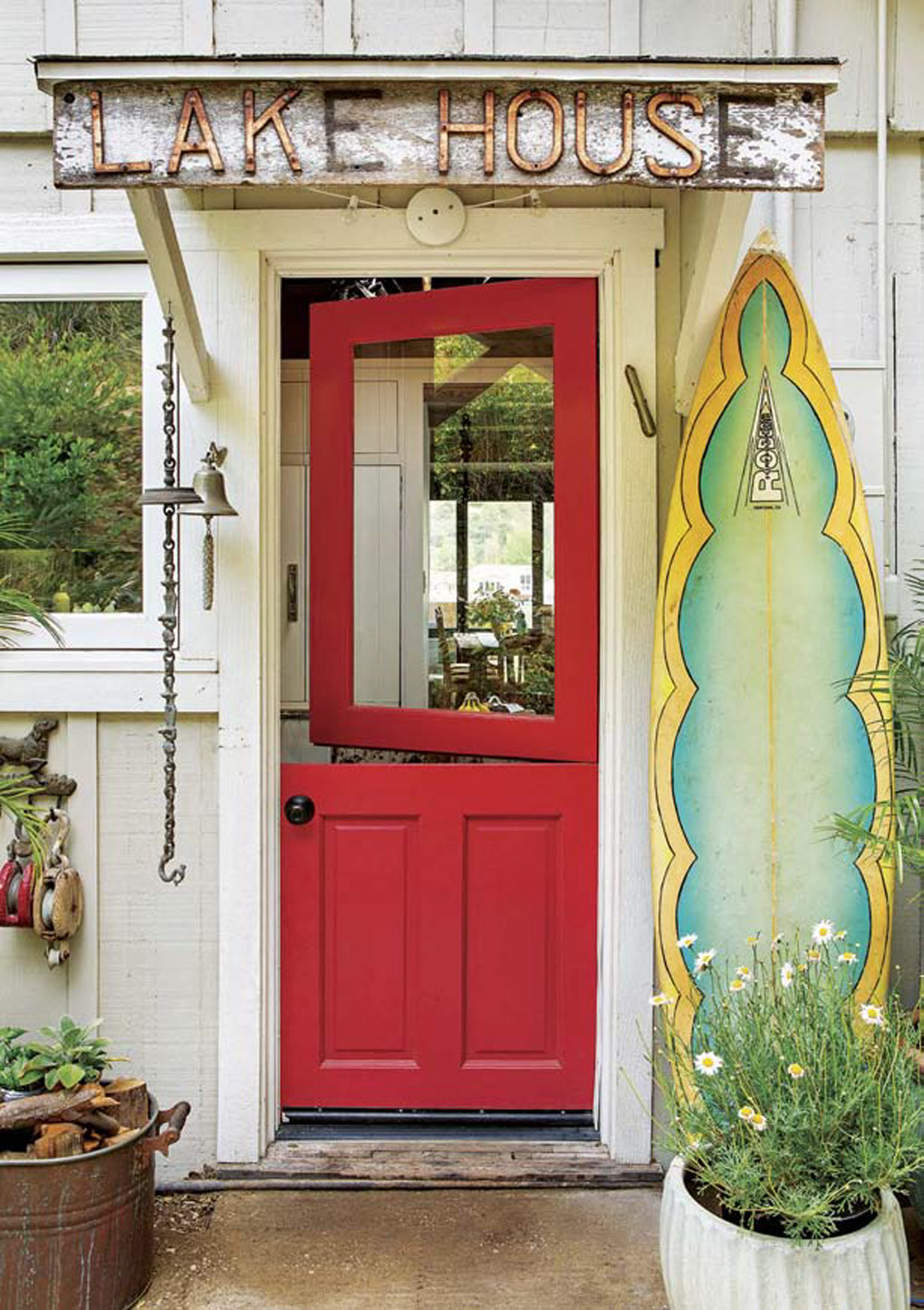 Vintage sign that reads "lake house" placed above a bright red front door on a porch covered in lake house decor. 