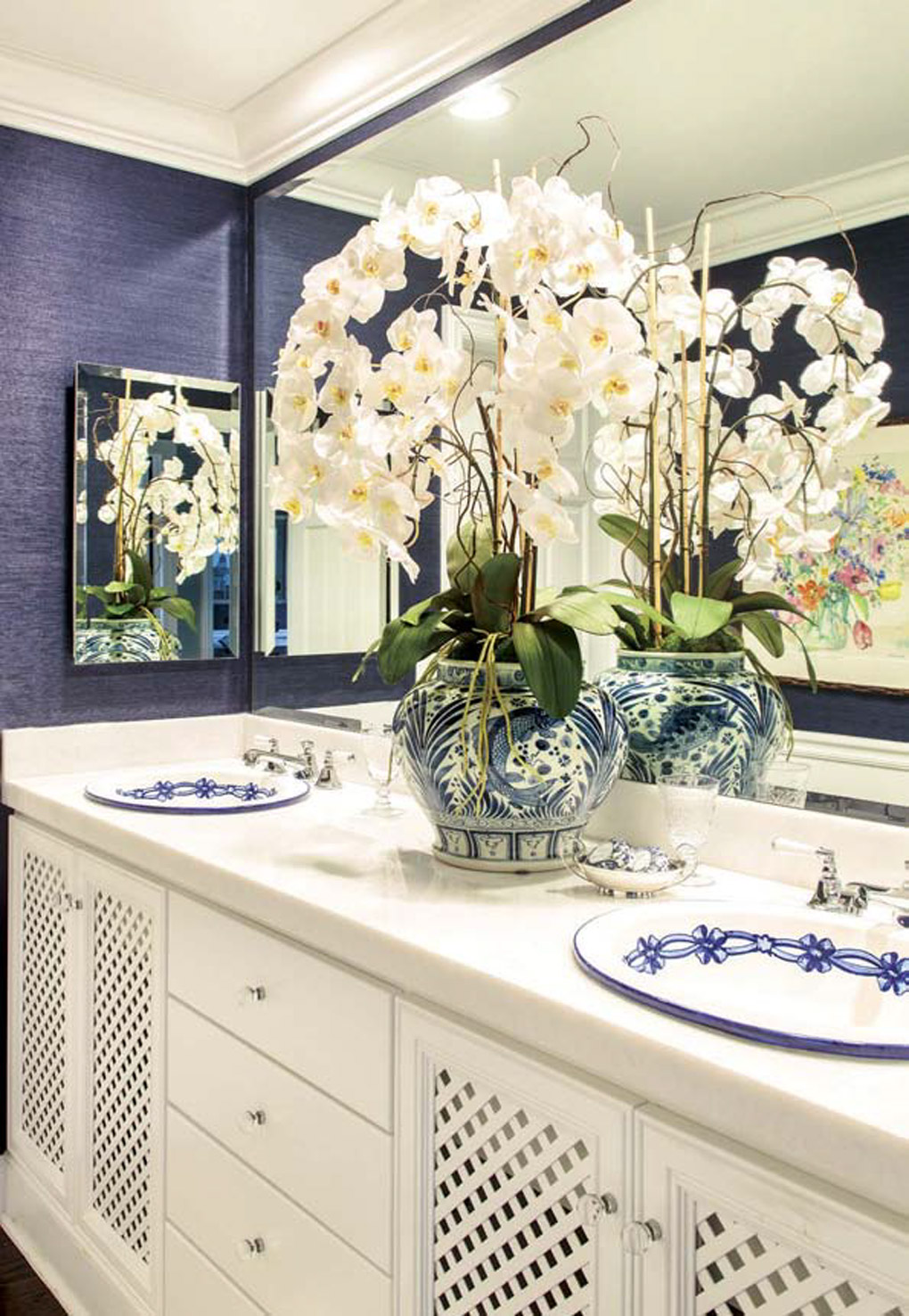 Blue and white Spanish sinks inlaid on a white double vanity in a bathroom topped with an oriental vase filled with white orchids. 