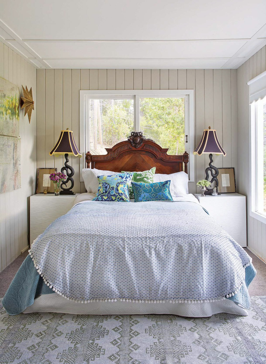 Master bedroom with 1940s vintage millwork around the walls and ceiling, light blue bedding and snake andirons turned lamps on the bedside tables. 