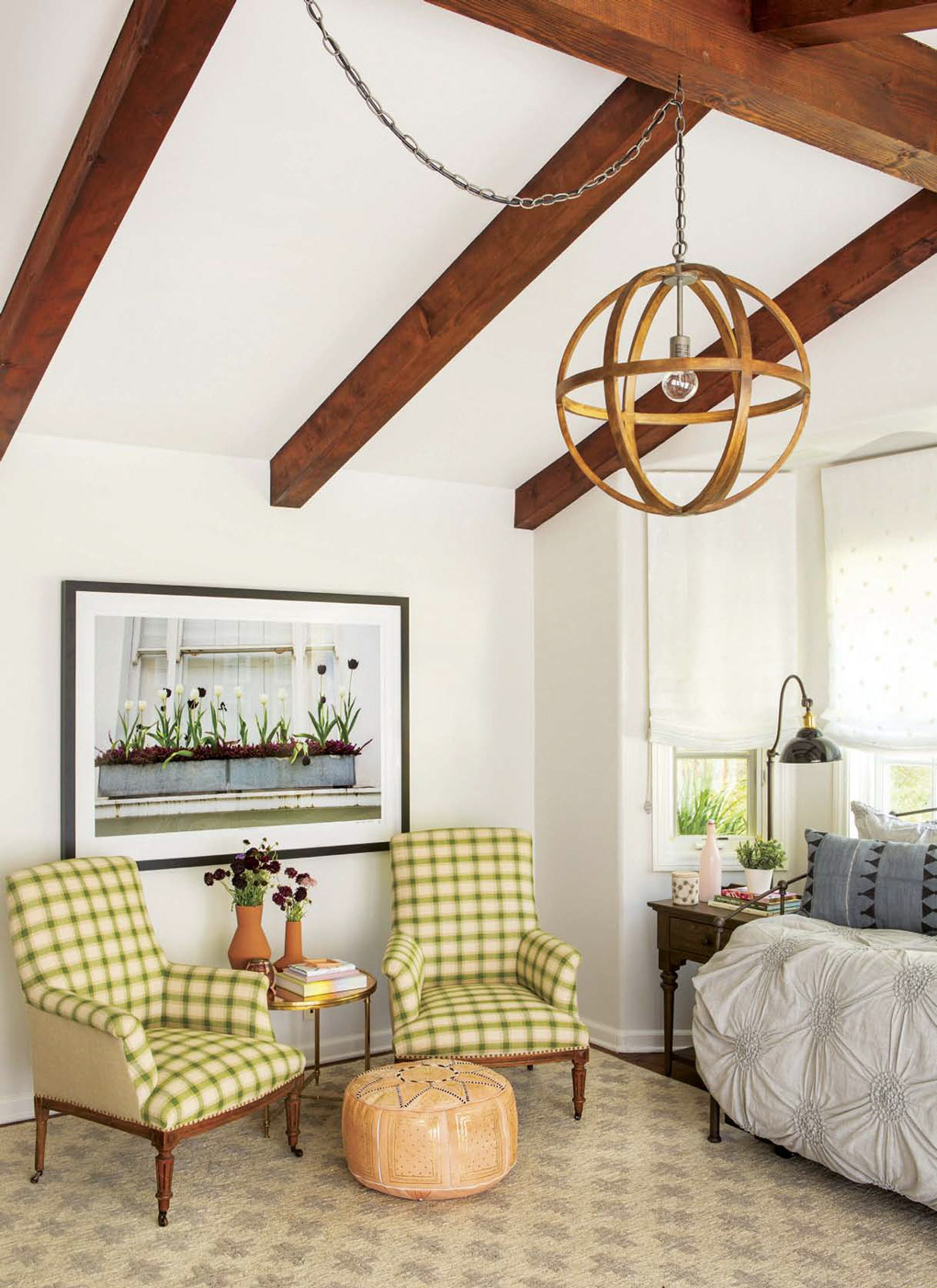 California cottage with bold exposed beams with a circular chandelier placed above green checkered armchairs. 