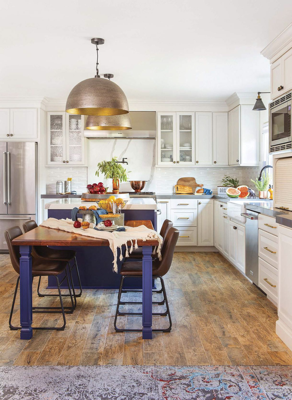 Kitchen remodel with white cabinet lined kitchen with a custom island and attached table with oversized hanging metal pendant lights. 