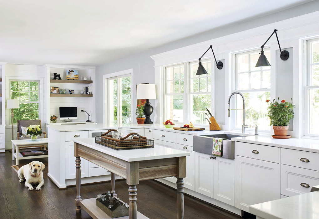 Remodeled white kitchen with freestanding island, looking over the counter into a living area with a large white dog resting on the floor. 