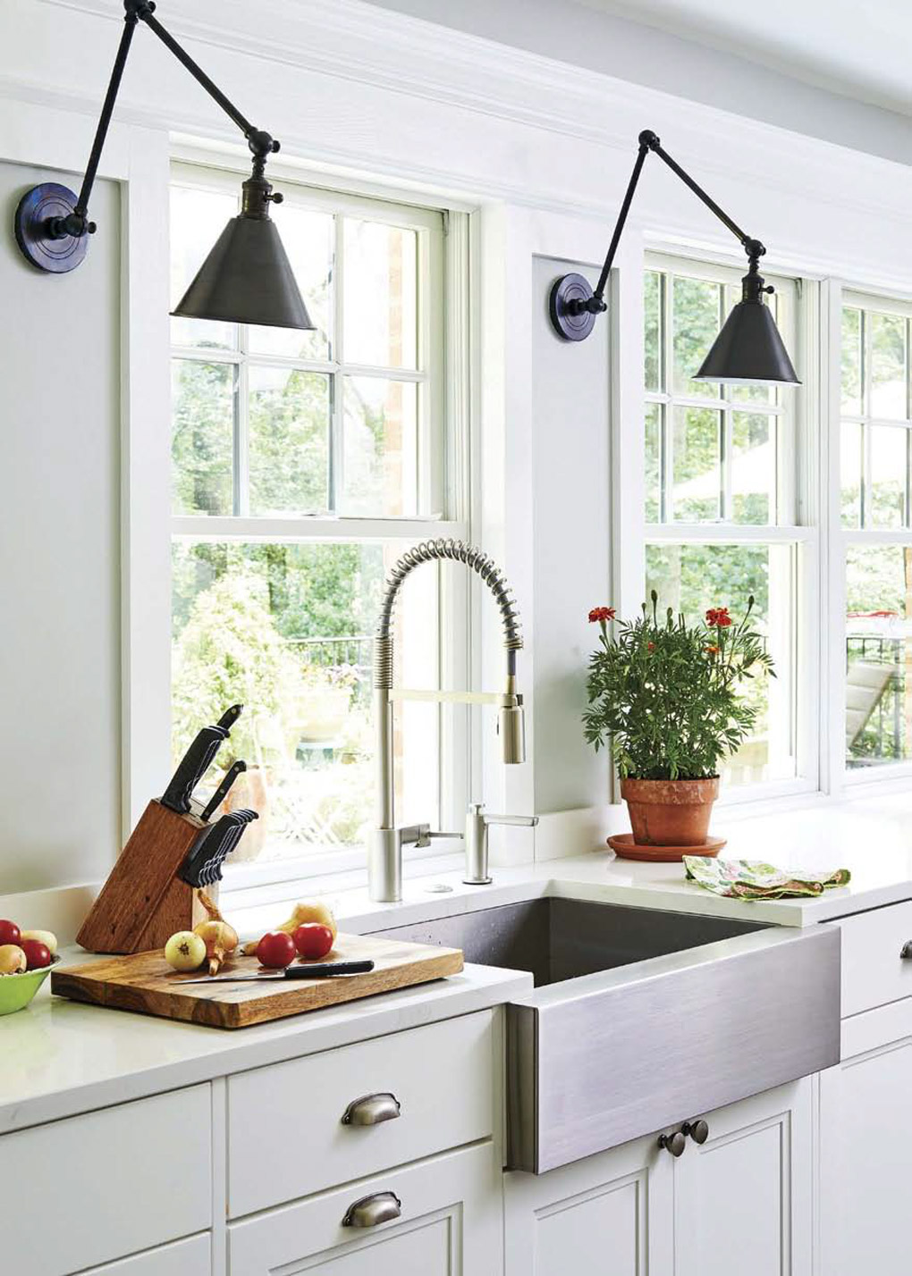 White kitchen with chrome farmhouse sink, chef's faucet and cutting board with fresh fruit.