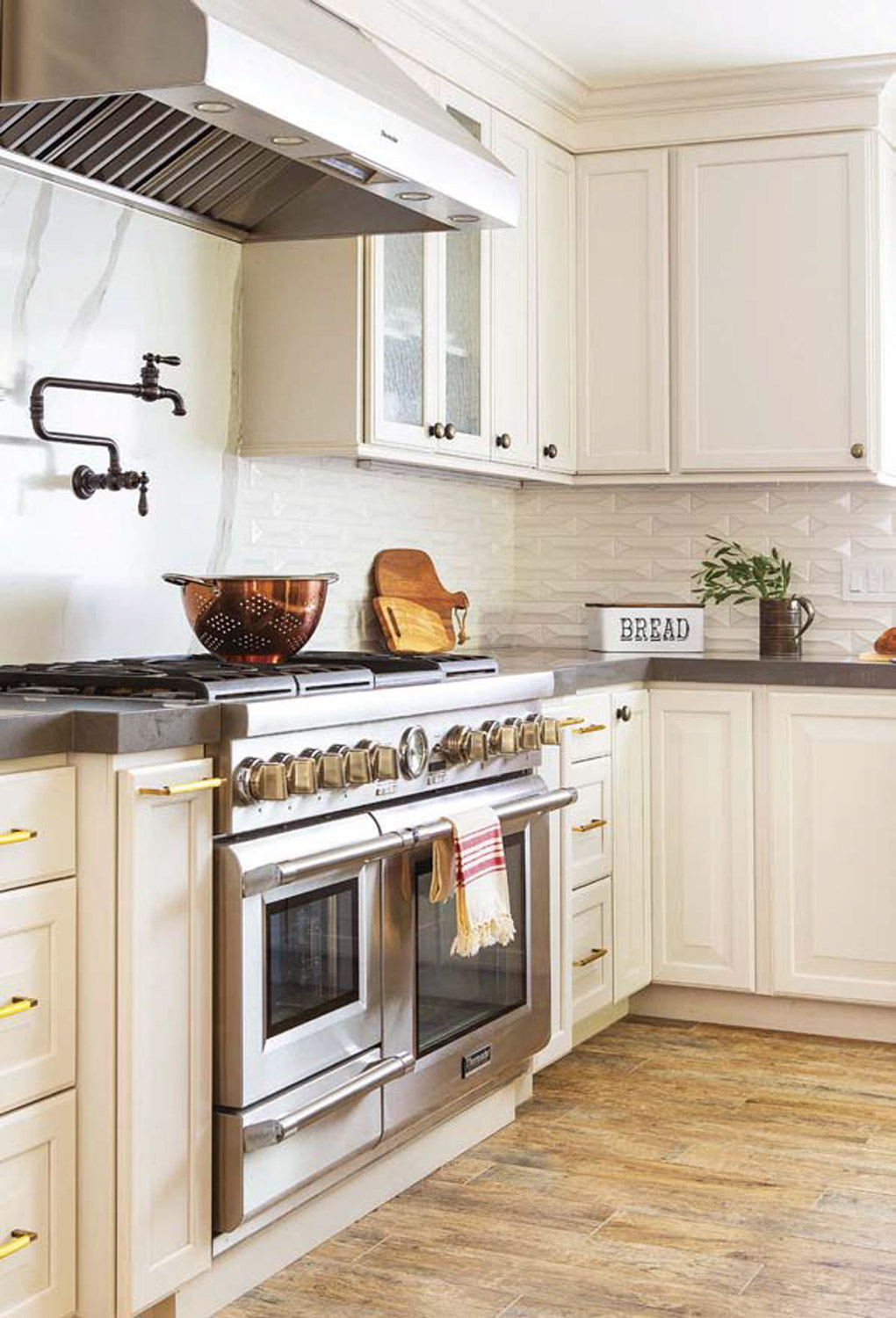 Kitchen remodel with Large chrome range with matching range hood in a custom cream cabinet lined kitchen. 