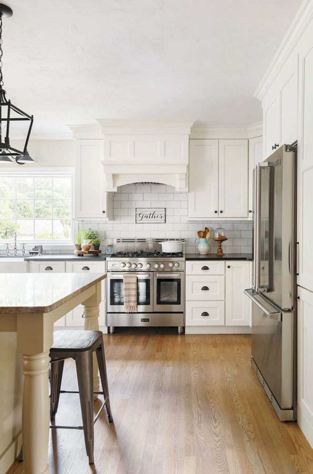 White kitchen with rustic cabinetry, oil-rubbed bronze pendant lights above the island and stainless steel appliances. 