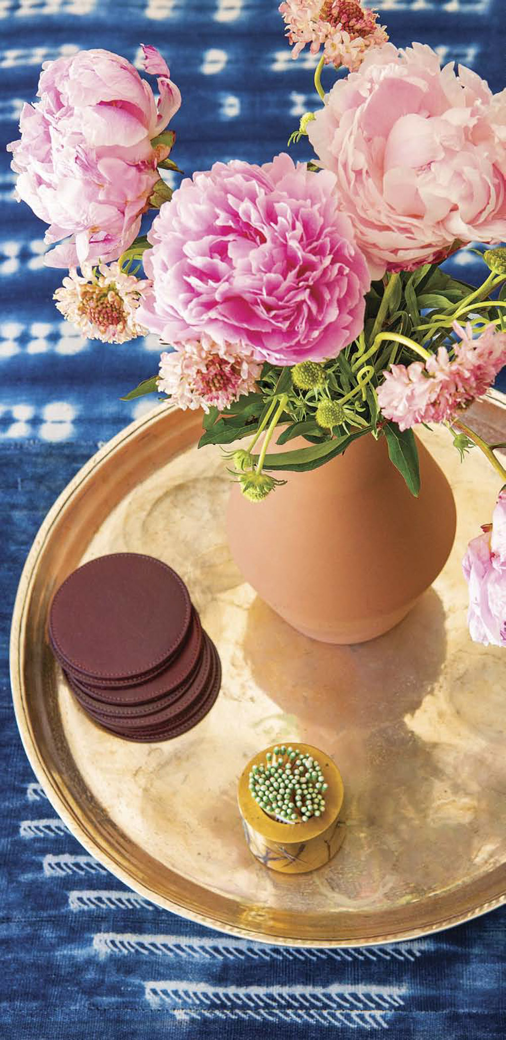 Shibori fabric covered coffee table topped with a gold tray and terra cotta pot filled with bright pink peonies. 