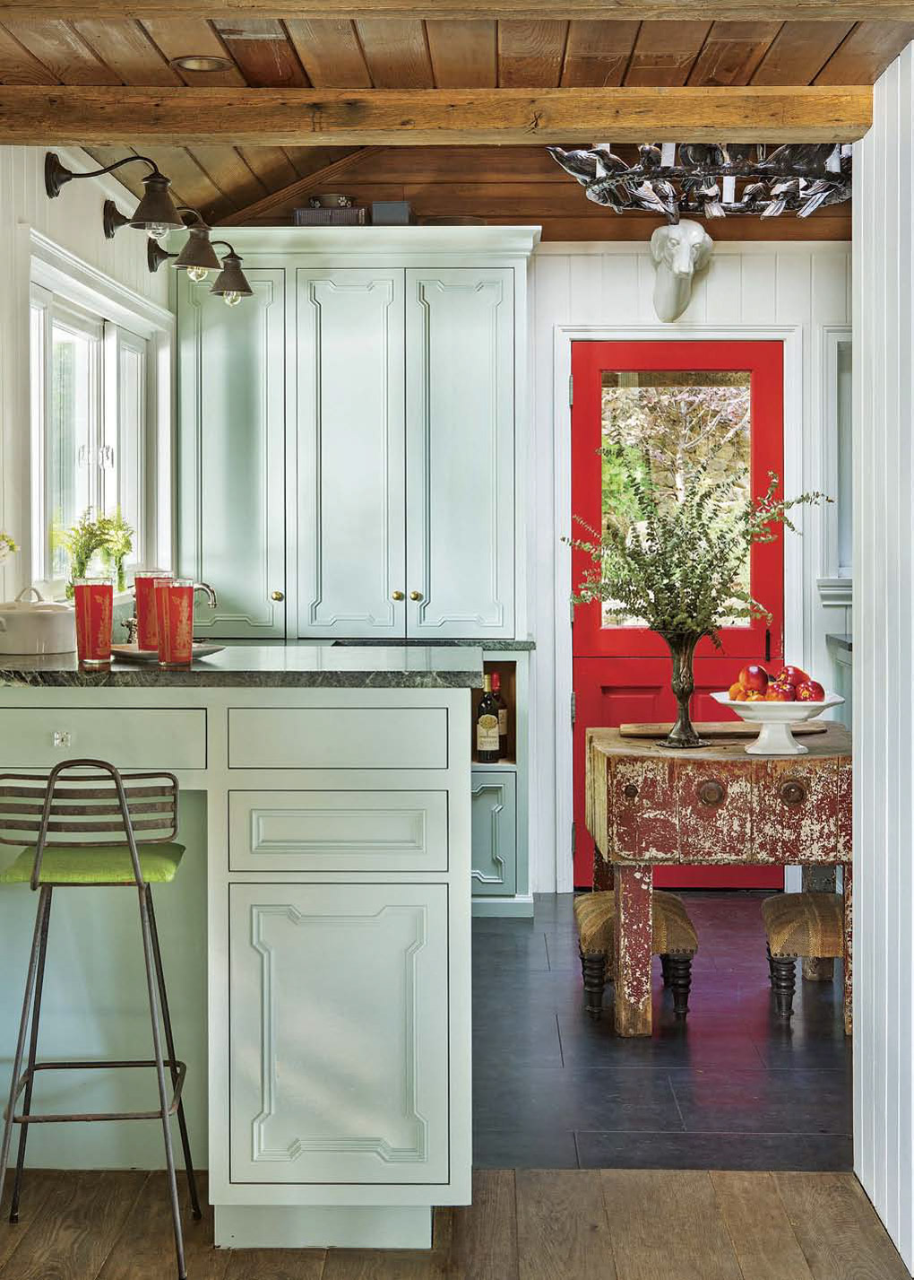 Light aqua cabinets in a kitchen with exposed beam ceilings and a bright red dutch door. 