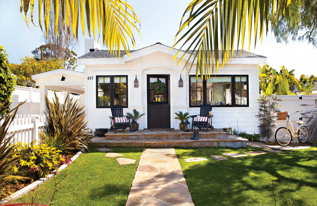 Pathway up to a white cottage with black accents around windows and the door.