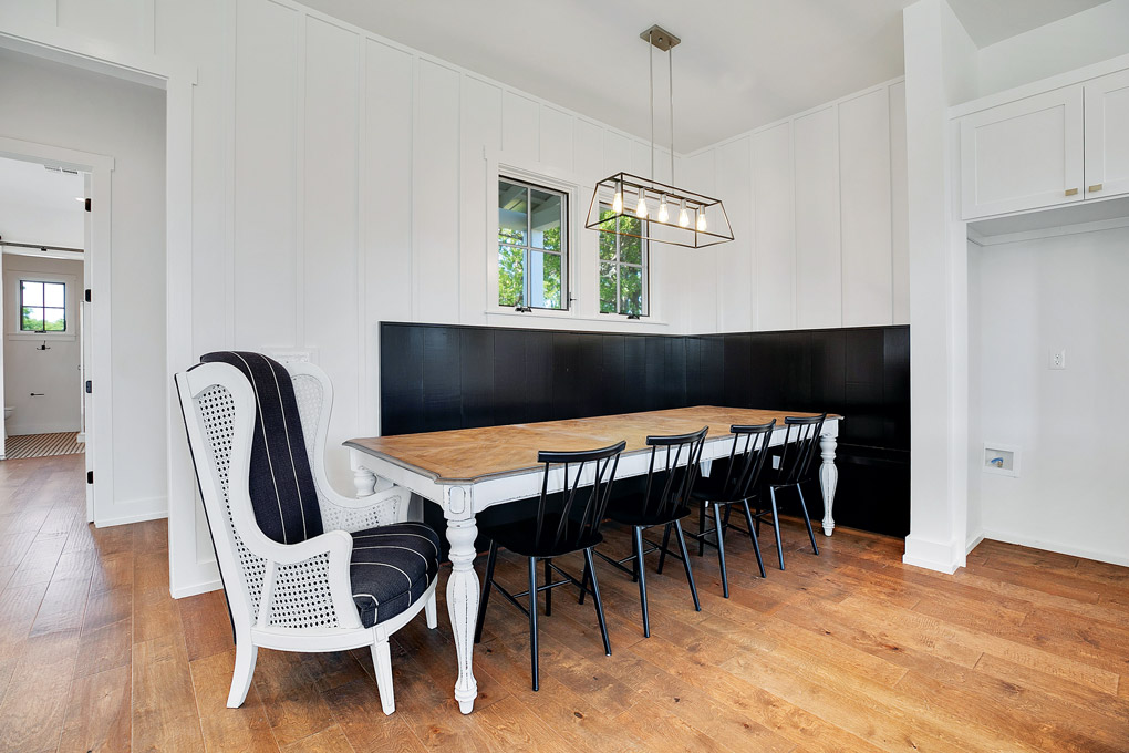 a black and white breakfast nook with a long far table and a wingback chair with cane panels.