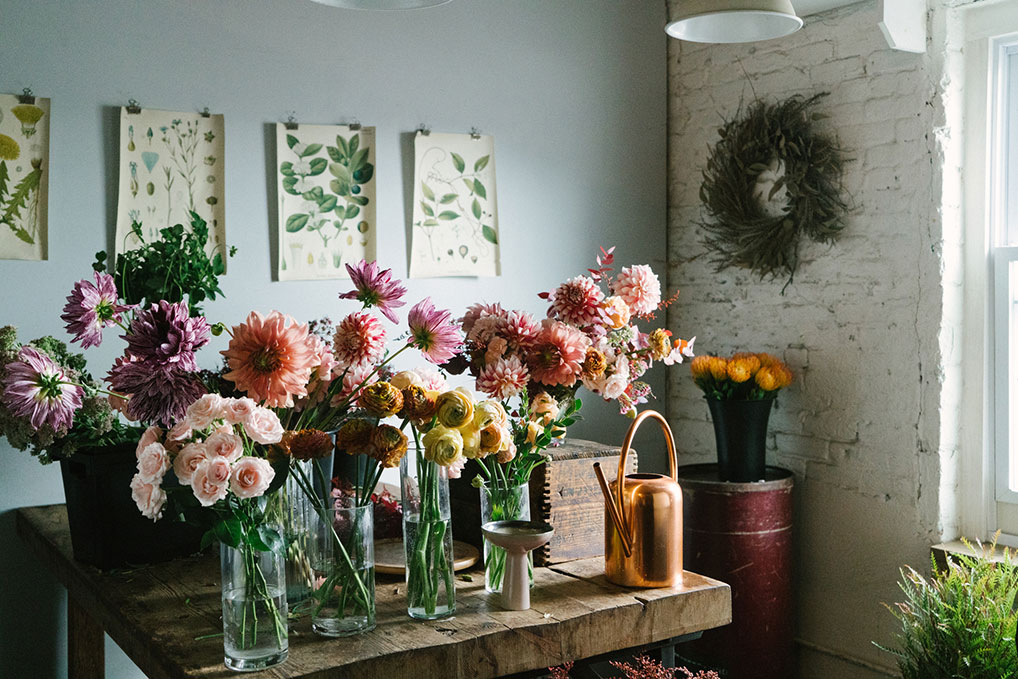 Floral design room with a wooden table covered in vases of flowers prepared to be placed in larger flower arrangements. 