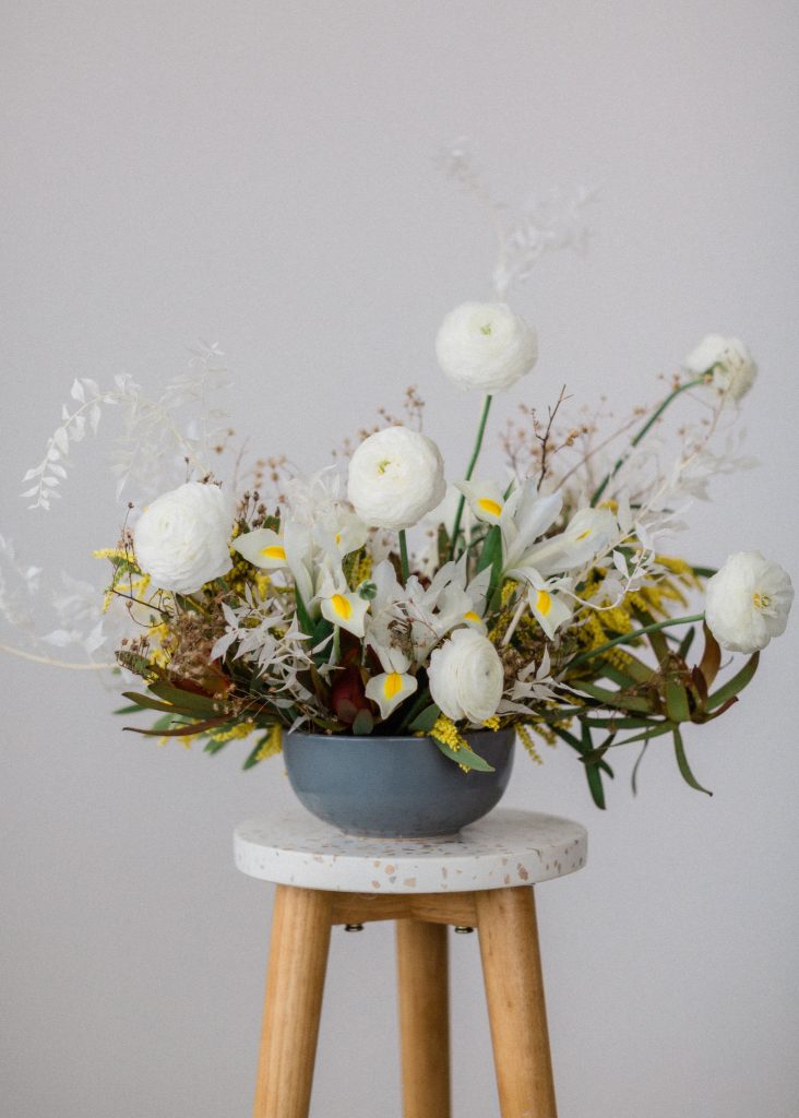 A Styled mid century modern floral design with a clean white wall with the flowers sitting on a simple stool