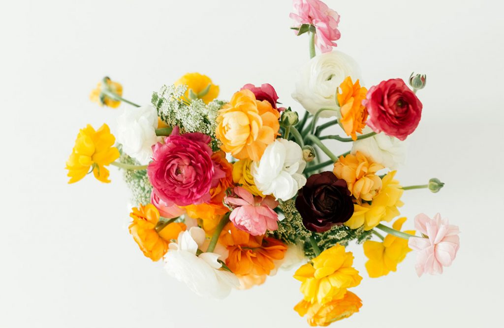 Overhead shot of a vibrant flower arrangement of peonies on a white table. 